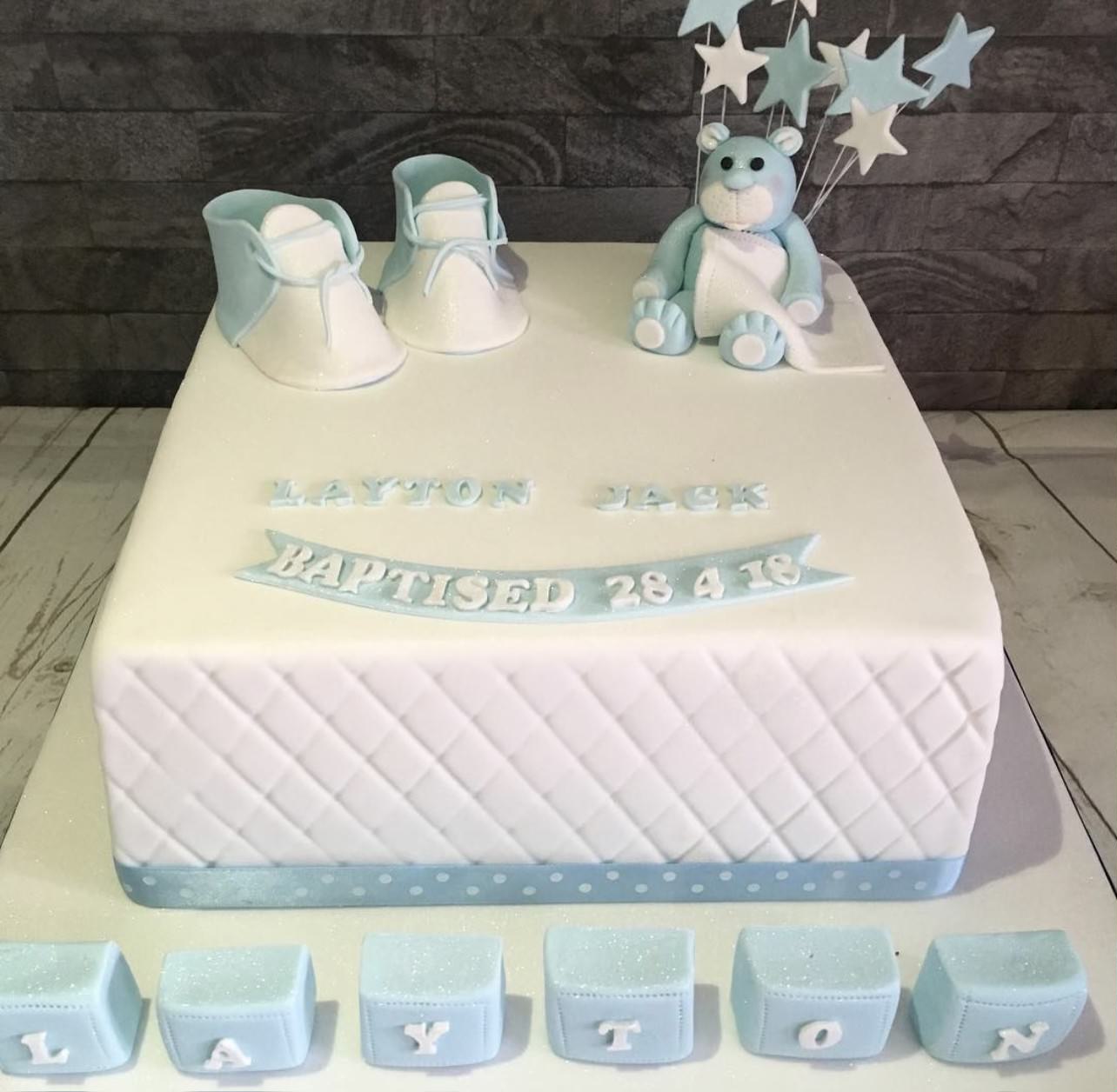 A white and light blue baptism cake with baby shoes