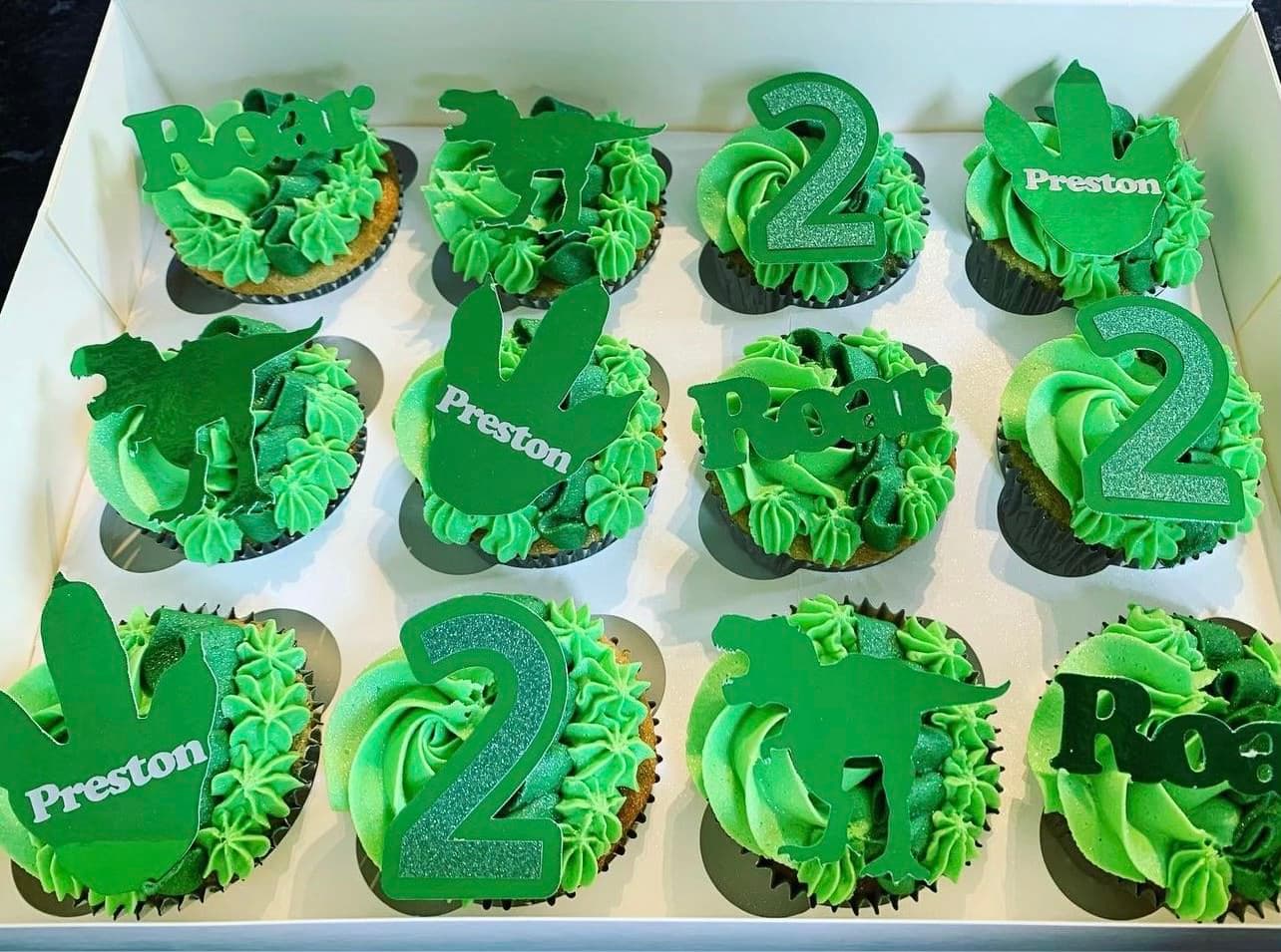 Green frosted cupcakes with dinosaur shapes on top for a second birthday