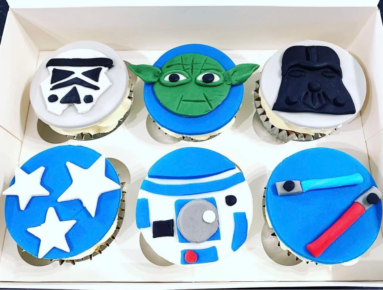 Blue and white cupcakes with a fondant storm trooper, yoda, darth vader, R2-D2 and lightsabers on top