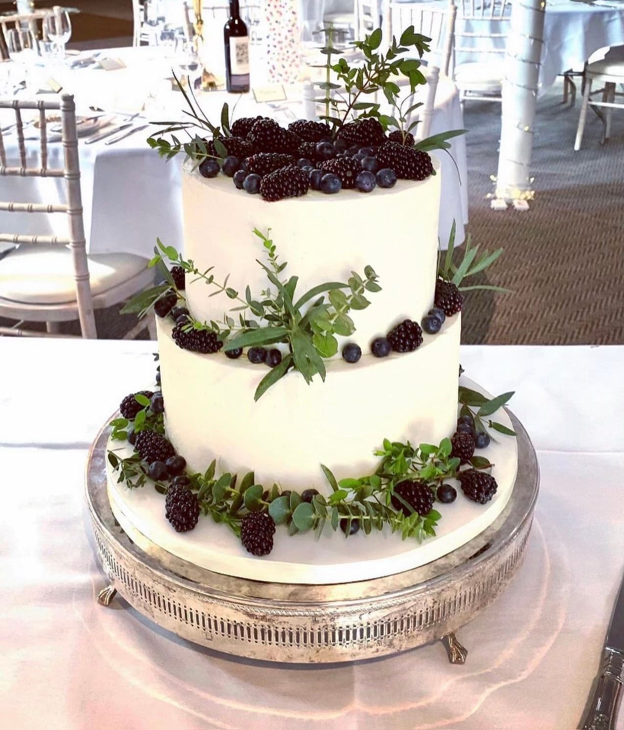 White natural wedding cake with blackberries, blueberries, foliage and a marble base
